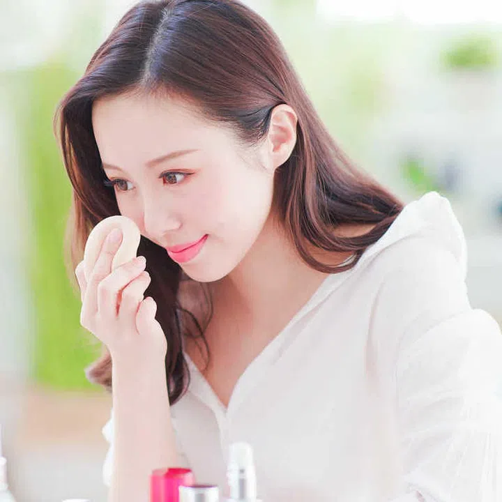 Beautiful asian woman using cosmetic sponge on face and look mirror at home