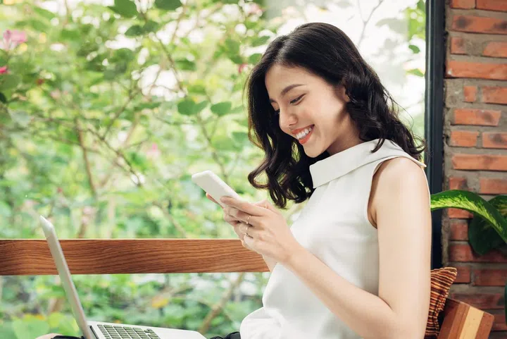 Confident young asian woman in smart casual wear typing on phone.
