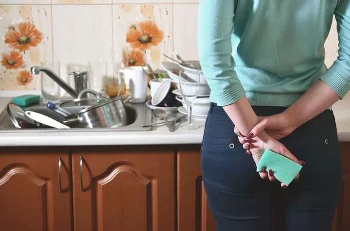 Fragment of the female body at the kitchen counter, filled with a lot of unwashed dishes. The girl is tired of coping with the daily duty of washing dishes. Problems of family life
