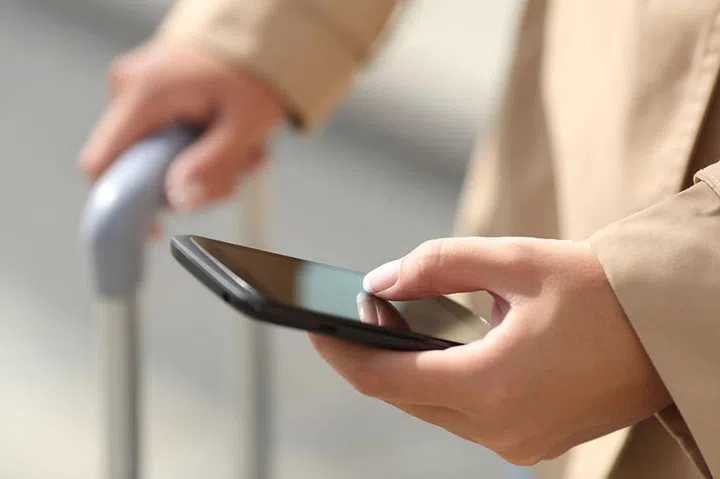 Close up of a traveler woman hand consulting a smartphone and holding a suit case