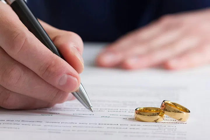 Hands of wife, husband signing decree of divorce, dissolution, canceling marriage, legal separation documents, filing divorce papers or premarital agreement prepared by lawyer. Wedding ring.
