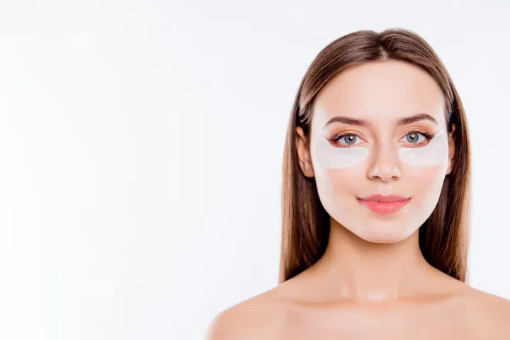 Close up portrait with copy space of pretty charming girl using applying patches under eyes fighting with dark circles isolated over white background. Wellbeing purity advertisement concept