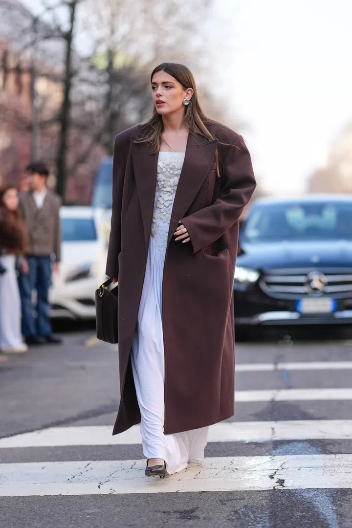 MILAN, ITALY - FEBRUARY 27: A guest wears a brown long coat, a white dress, a brown leather bag, shiny black leather pointed shoes, outside Max Mara, during the Milan Fashion week Women's Fall/Winter 2025-2026 on February 27, 2025 in Milan, Italy. (Photo by Edward Berthelot/Getty Images)
