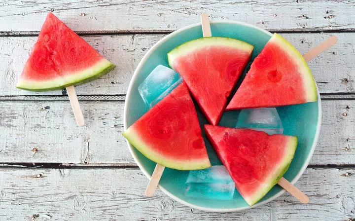 57081359 - watermelon slice popsicles on a vintage blue plate and rustic wood background