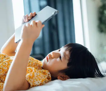 Girl lying down on bed using ipad