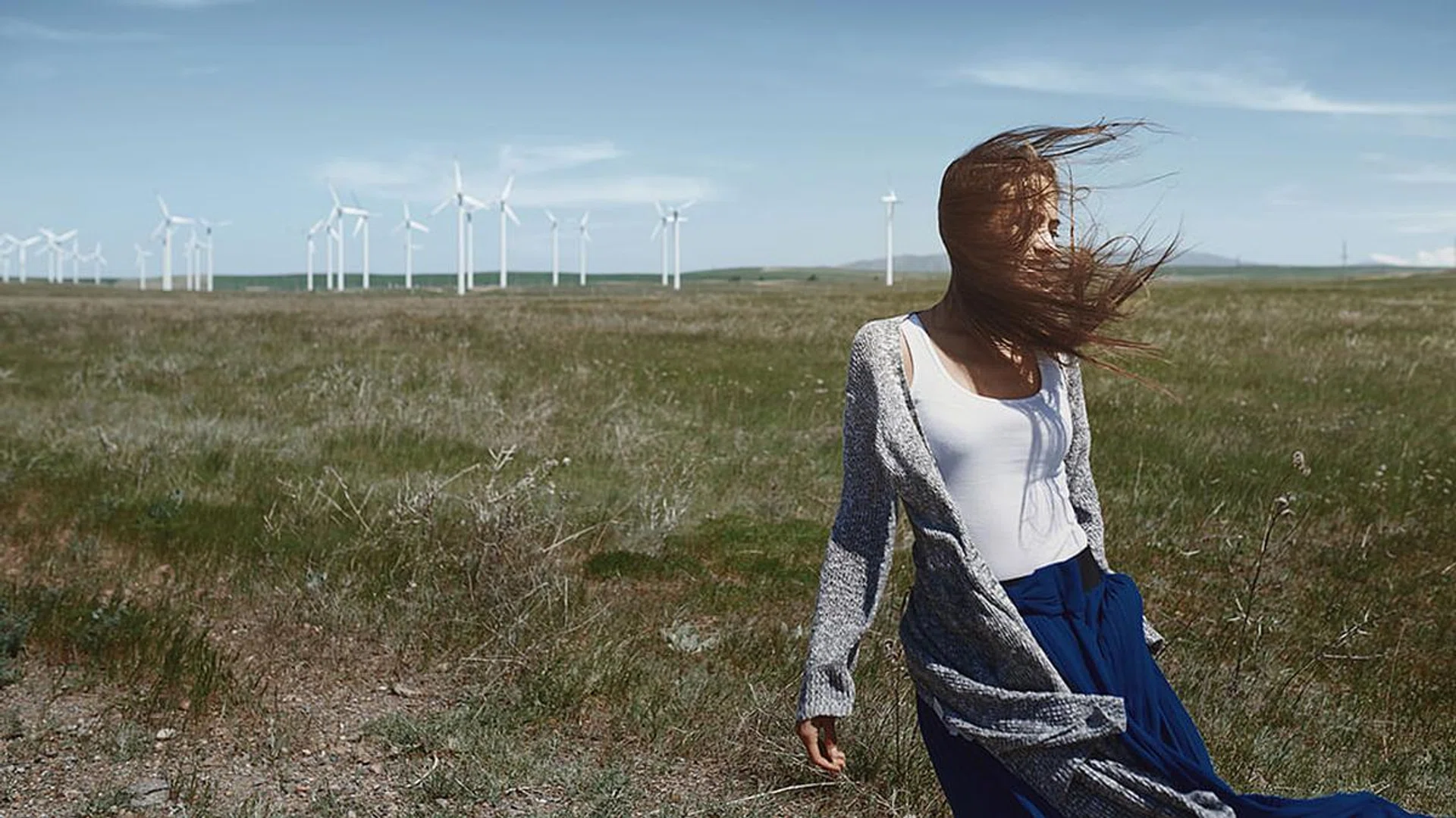 Woman with long tousled hair next to the wind turbine with the wind blowing