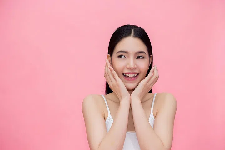 Excited and surprised smiling Asian 20s woman isolated over pink background