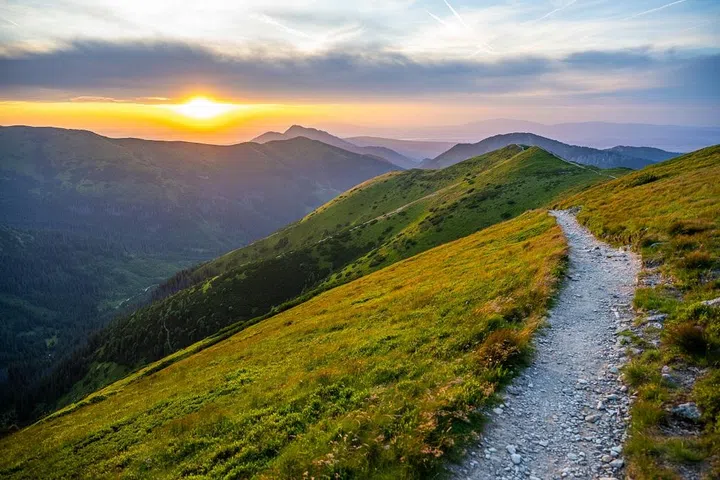 Trekking path in the mountains during beautiful summer sunset. Sun shining through the colorful clouds.