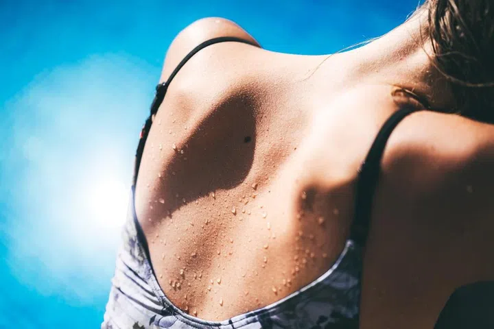 Beautiful tanned woman's back, exposed to the sun, the lady is wearing a swimsuit and sunbathing. Necessity of sun protection. Consequences of UV light, skin cancer prevention, and barrier health