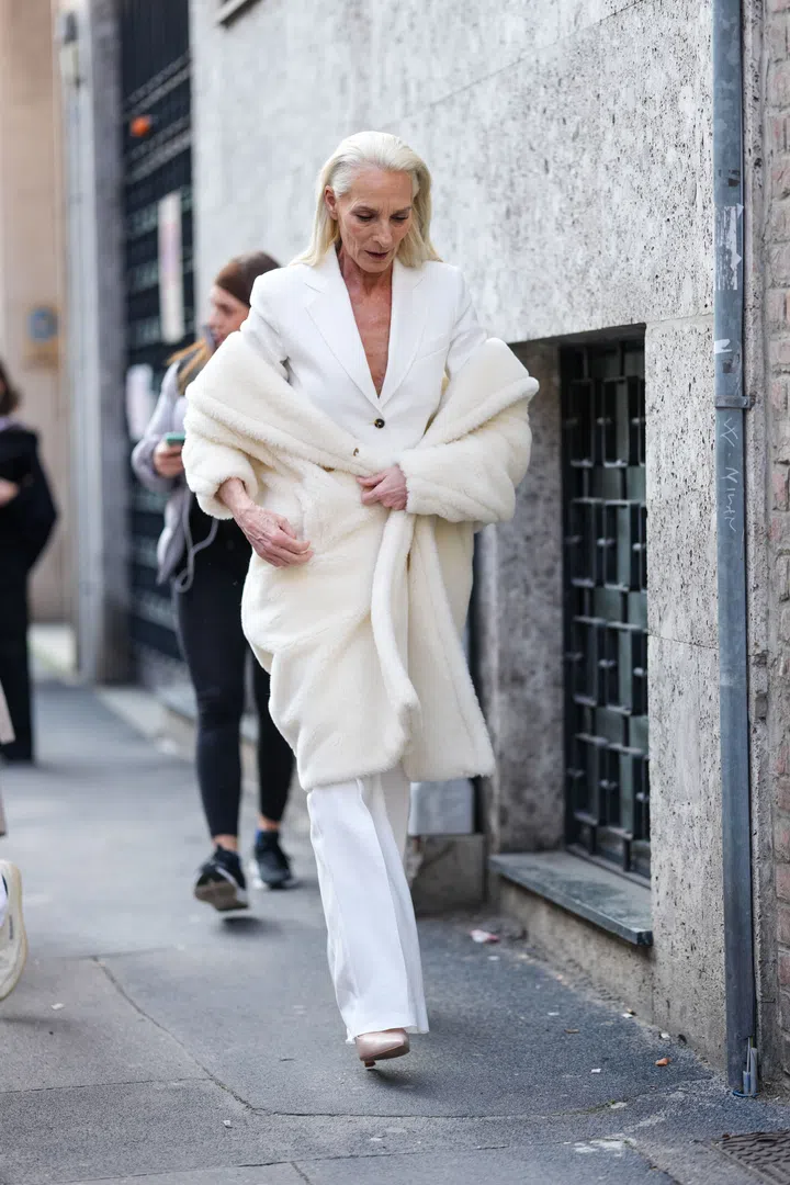 MILAN, ITALY - FEBRUARY 27: A guest wears white blazer jacket, cream teddy bear Max Mara coat, white trouser pants, light brown pointed toe heels leather shoes, outside Max Mara, during the Milan Fashion week Women's Fall/Winter 2025-2026 on February 27, 2025 in Milan, Italy. (Photo by Edward Berthelot/Getty Images)