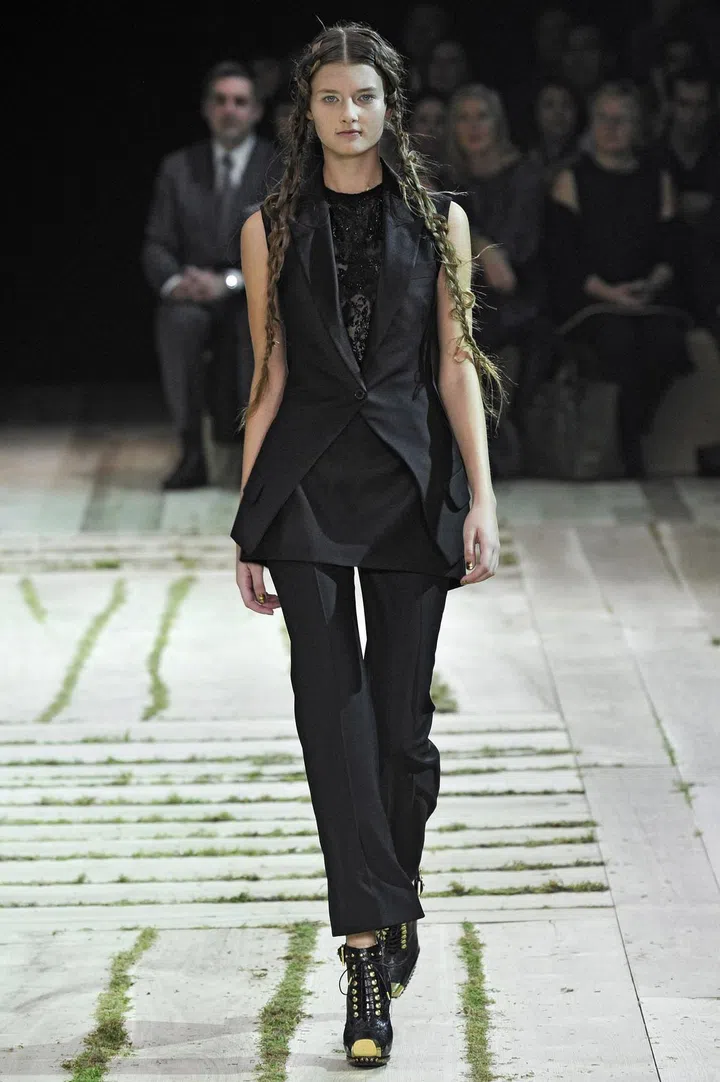 A sleeveless tailored tuxedo jacket with a cutaway front, tonal satin lapels, a single button fastening, two faux flap pockets, a double inverted box pleat at the reverse hem and a vent at centre back in black wool, from the Alexander McQueen Spring/Summer 2011 collection.