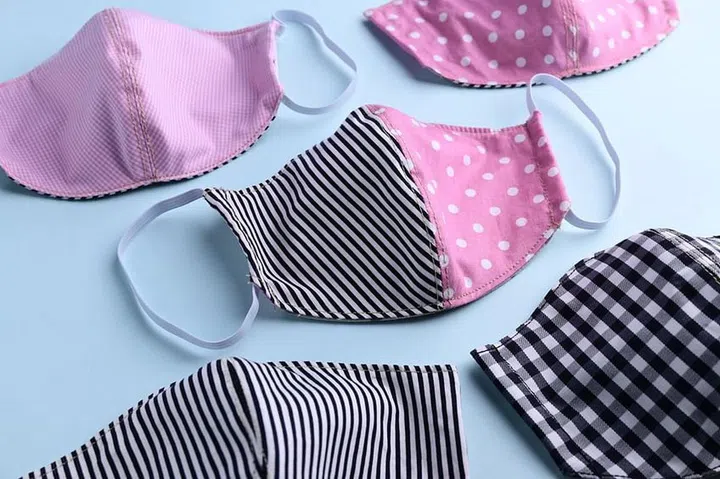 flat lay design of black and pink colorful fashion face mask handmade from fabric cloth on blue background