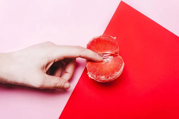 Concept sex, masturbation. Hand, fingers in grapefruit, vagina symbol on a red background