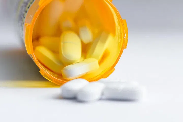 close up of a group of white tablets with an out of focus prescription bottle in the background