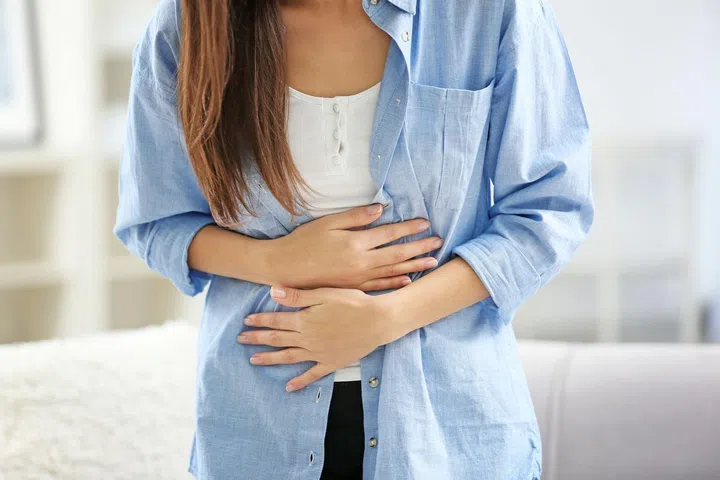 Young woman suffering from abdominal pain at home, closeup. Gynecology concept