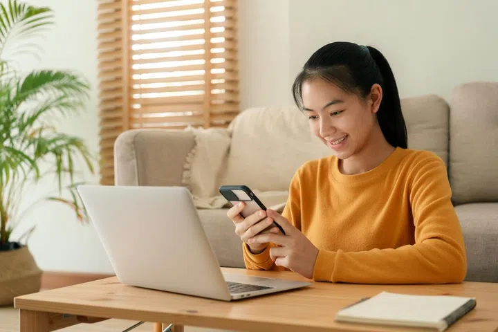 Beautiful Asian women wear long sleeve yellow using text message mobile phone. happy young woman using a phone smile on the face while sitting in living room at home morning