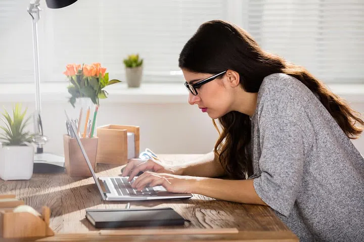 Businesswoman Sitting In Wrong Posture Working On Laptop On Wooden Office Desk