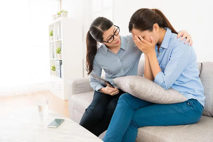 sadness depressed woman having psychology problem sitting on sofa crying and her doctor adviser looking at her trying to comfort.