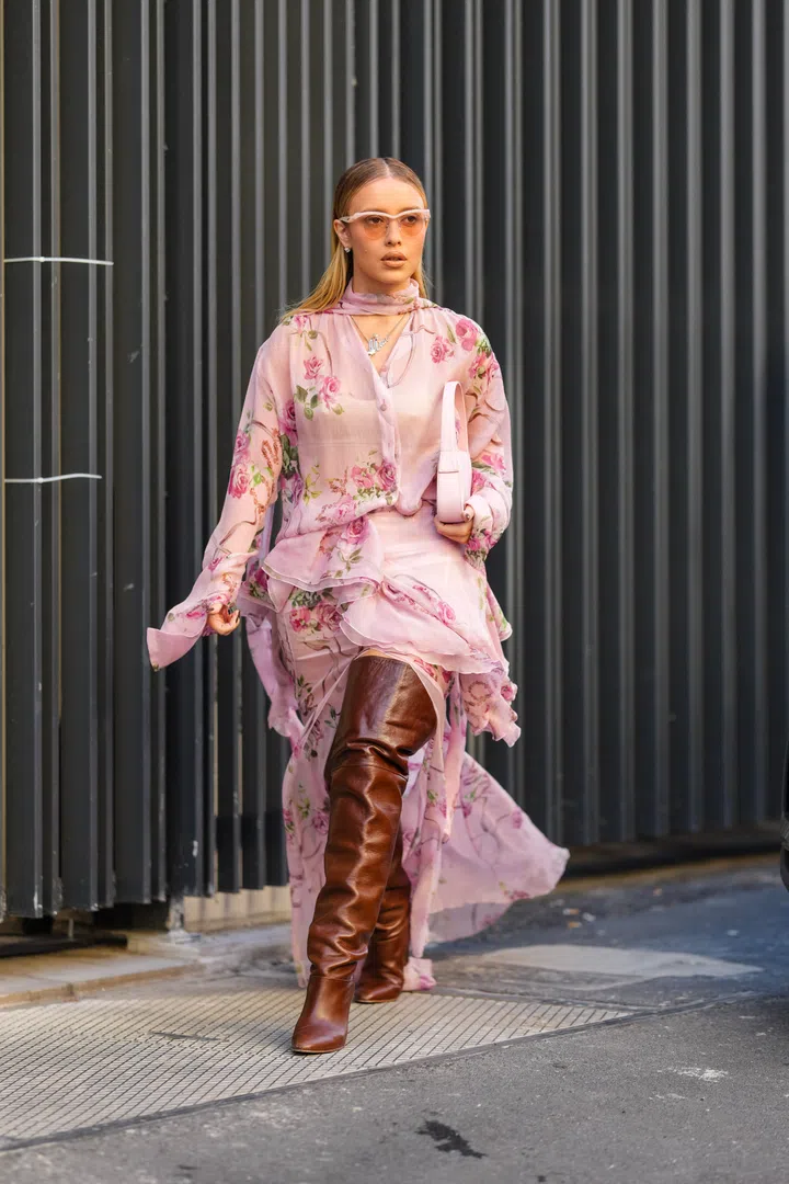 MILAN, ITALY - FEBRUARY 27: A guest wears light pink sunglasses, silver statement necklace, light pink sheer mesh rose floral pattern/print buttoned up long sleeve flowy shirt, light pink sheer mesh rose floral pattern/print layered flowy midi skirt, shiny dark brown thigh high pointed toe slouchy heels leather shoes, light pink leather bag, outside Blumarine, during the Milan Fashion week Women's Fall/Winter 2025-2026 on February 27, 2025 in Milan, Italy. (Photo by Edward Berthelot/Getty Images)