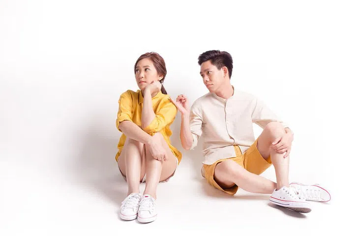 Young sulky asian female and young man trying to reconcile. sitting on white background