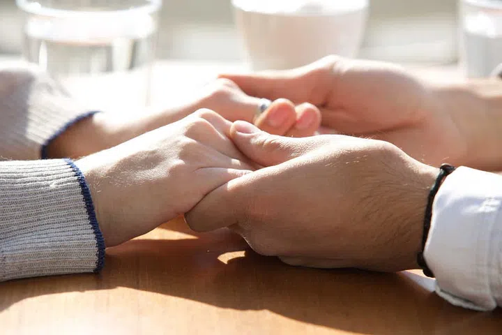 Close up male and female holding hands over table
