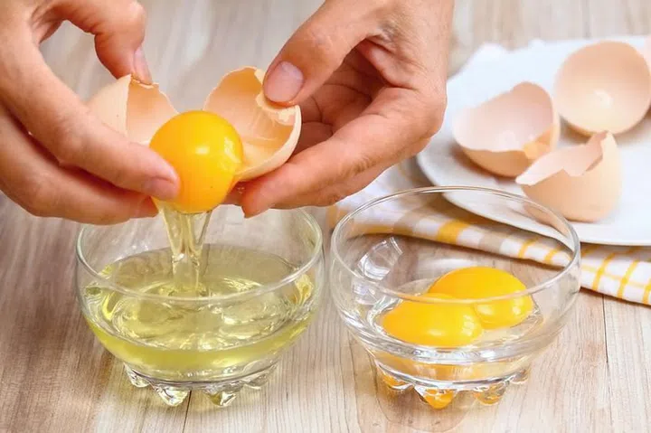 Woman hands breaking an egg to separate  egg- white and  yolks and egg shells at the background