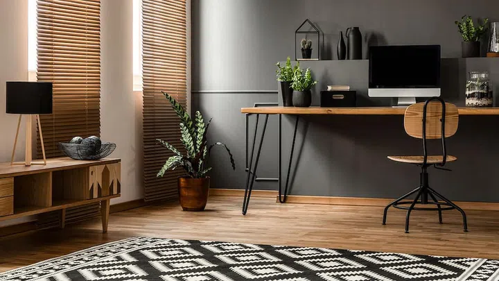 Lamp on wooden cupboard near plant and desk with computer monitor in dark grey workspace interior