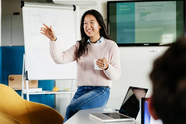 A cheerful office employee giving a presentation to her peers in a modern works space.