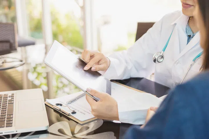 Female Doctor consulting  and discussing records with female patient, presenting results on tablet computer, sitting at desk., selective focus, vintage color