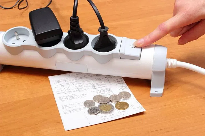 Finger of woman turns off electrical extension, electrical plugs connected to electrical power strip, electricity bill with coins, concept for energy saving