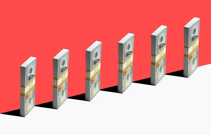 6 bundles of US $100 bills standing vertically on edge of white shelf, red background