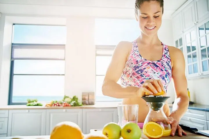 Happy sporty woman standing in sunlight in the kitchen making juice. Horizontal indoors shot