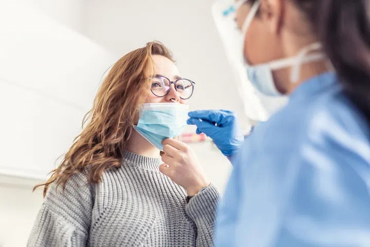 Smiling girl puts face mask off her nose so that a healthcare worker can take a sample for Covid-19 testing.