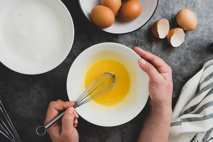 Woman's hands whisk eggs in bow. Cooking omlette for breakfast. Top view of cooking process. Dark background.