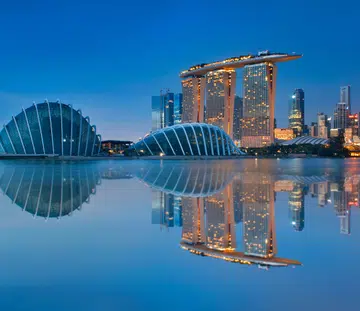 Gardens by the Bay and Singapore skyline reflection on blue water at blue hour in Singapore.