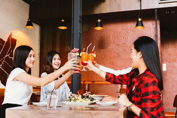 Group of Asian happy and smiling young man and women holding an alcoholic cocktail for toasting and celebrating in social party in restaurant
