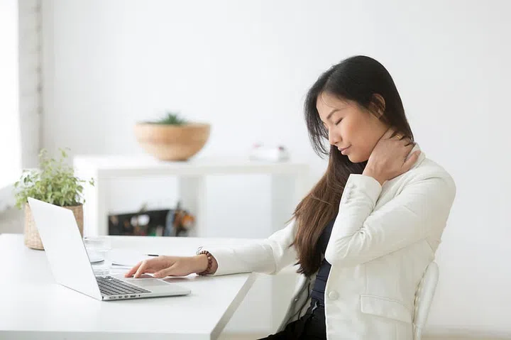 Young asian businesswoman touching massaging stiff neck to relieve pain in muscles after sedentary computer work in incorrect posture, japanese or chinese woman suffering from fibromyalgia at work
