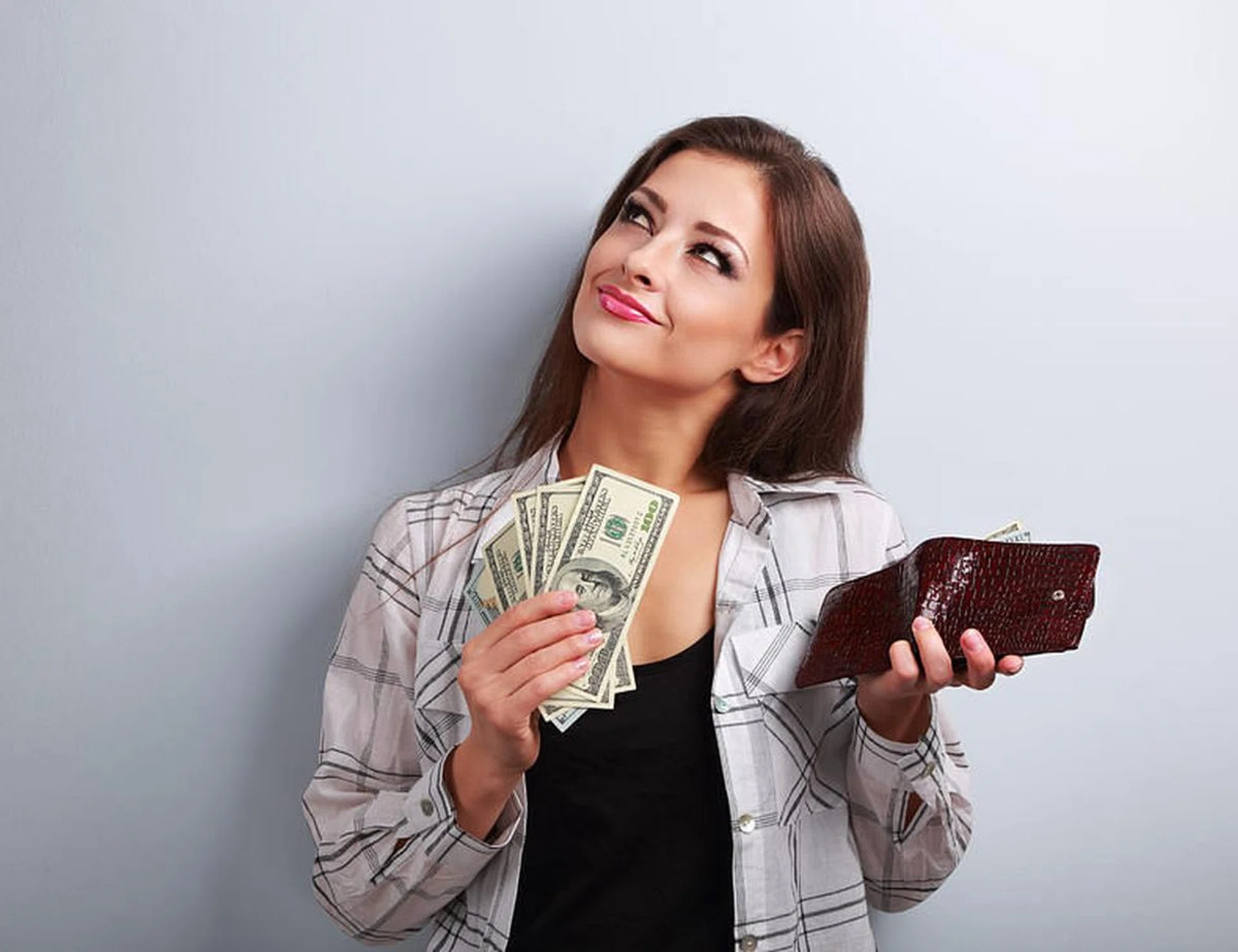 54410169 - thinking happy woman holding dollars and wallet in hands and want to spend money on blue background