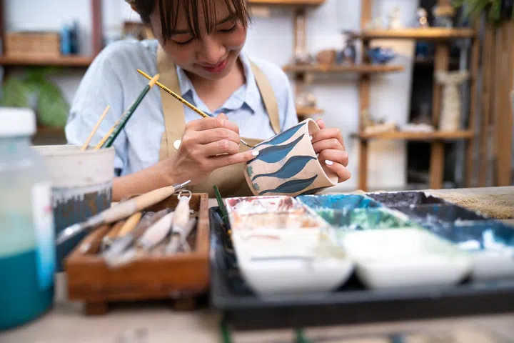 Woman coloring handmade Ceramic using brush and color,workshop production of ceramic tableware product painting
