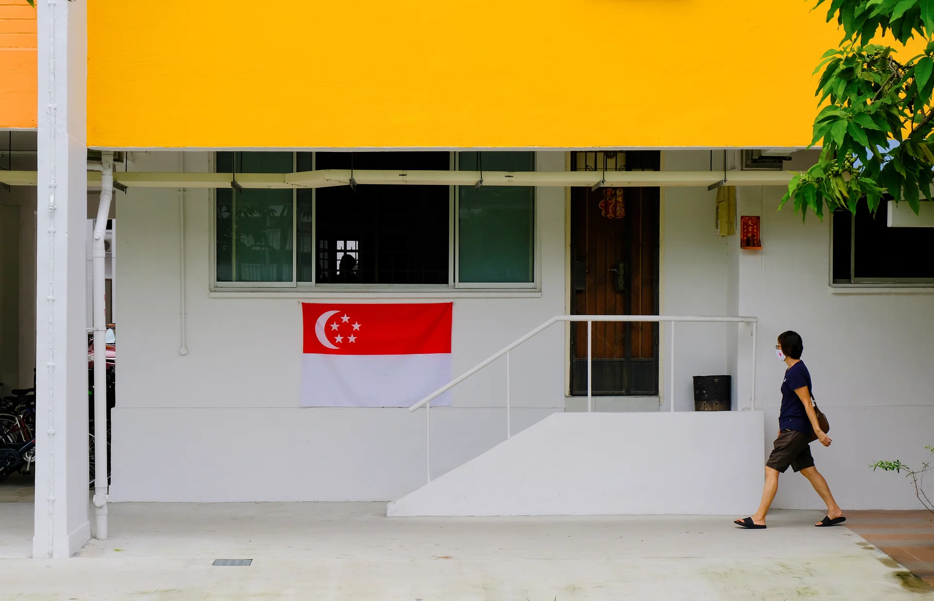 Singapore Jul 28 2020 Typical local heartland neighbourhood; Singapore flag hung outside apartment to welcome National Day on Aug 09. Asian woman in face mask walking past ground floor flat