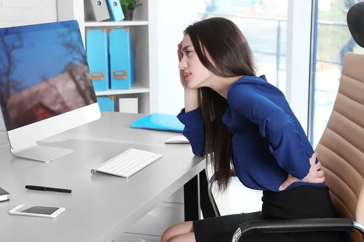 Posture concept. Young woman suffering from back pain while working with computer at office