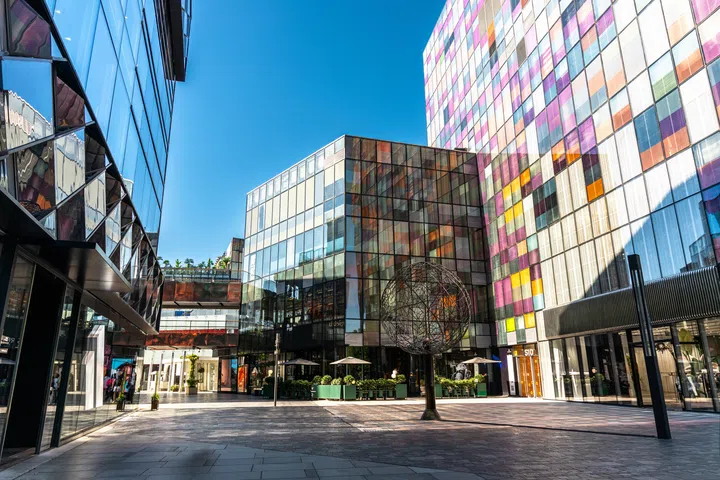 Modern shopping complex at open public Sanlitun Taikoo Li in Beijing, varied glass and colorful panel facades, spherical art sculpture on pedestrian street under clear blue sky, contemporary urban architecture.