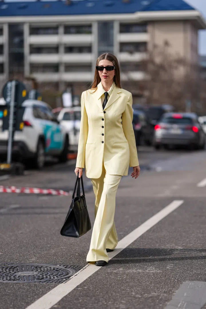 MILAN, ITALY - FEBRUARY 26: A guest wears black sunglasses, silver hairpins, light pale yellow buttoned up long sleeve shirt, black necktie, light pale yellow tailored Jil Sander blazer jacket, light pale yellow flared trouser pants, shiny black leather tote bag, black boots leather shoes, outside Jil Sander, during the Milan Fashion week Women's Fall/Winter 2025-2026 on February 26, 2025 in Milan, Italy. (Photo by Edward Berthelot/Getty Images)