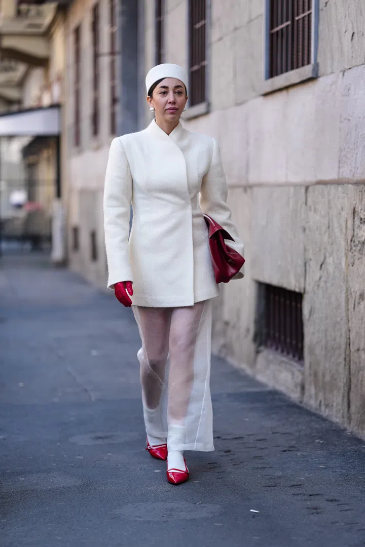 MILAN, ITALY - FEBRUARY 27: A guest wears white pill box hat, white earrings, cream wrapped blazer coat, shiny burgundy bordeaux leather bag, shiny burgundy bordeaux leather gloves, white sheer mesh midi skirt, white socks, shiny cherry red pointed toe slingback kitten heels leather shoes, outside Max Mara, during the Milan Fashion week Women's Fall/Winter 2025-2026 on February 27, 2025 in Milan, Italy. (Photo by Edward Berthelot/Getty Images)
