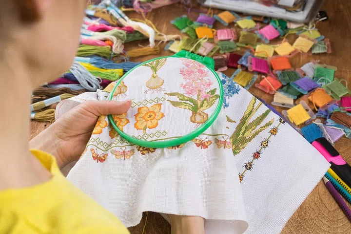 Girl sitting at a table where everything necessary for embroidery, embroiders a bigger picture. Copy paste
