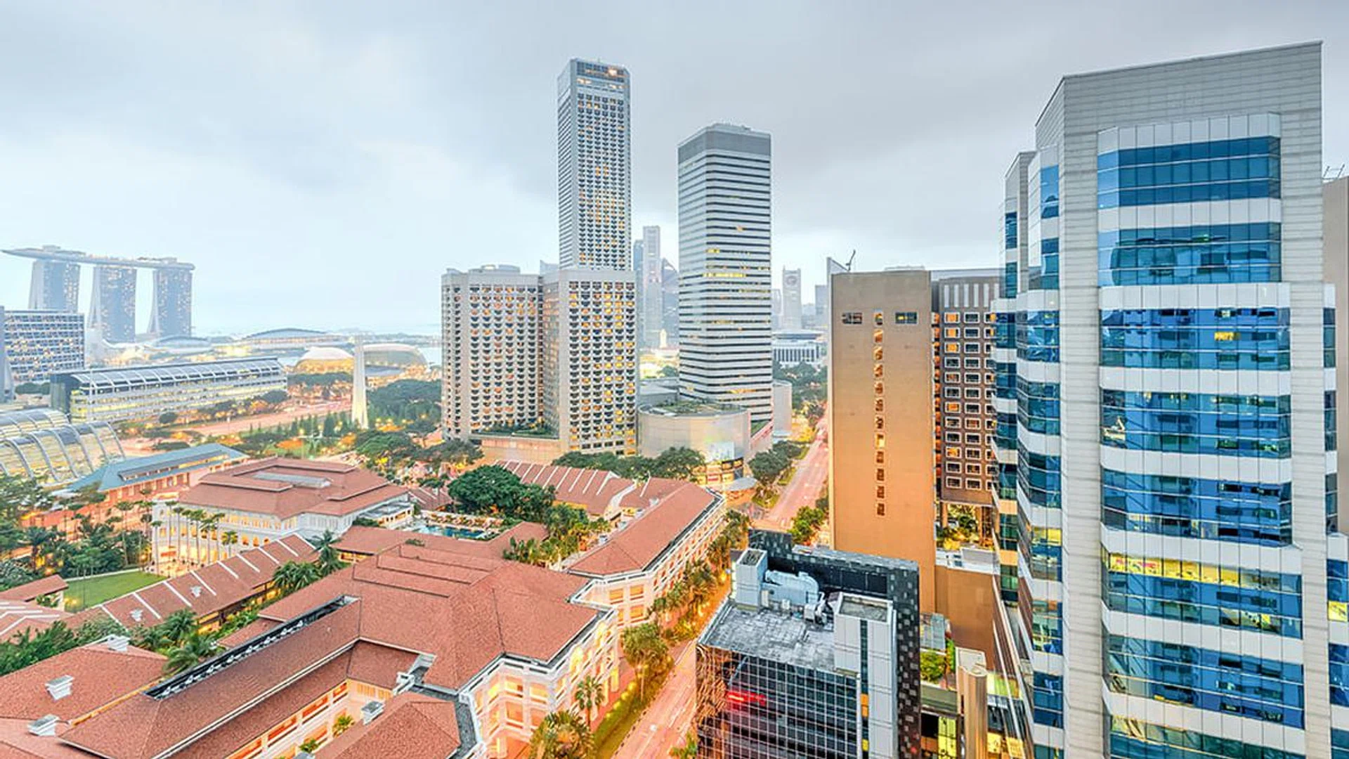 Aerial view office and residential buildings in downtown Singapore with skylines in background. Illuminated lights from skyscrapers and traffic on the main street.