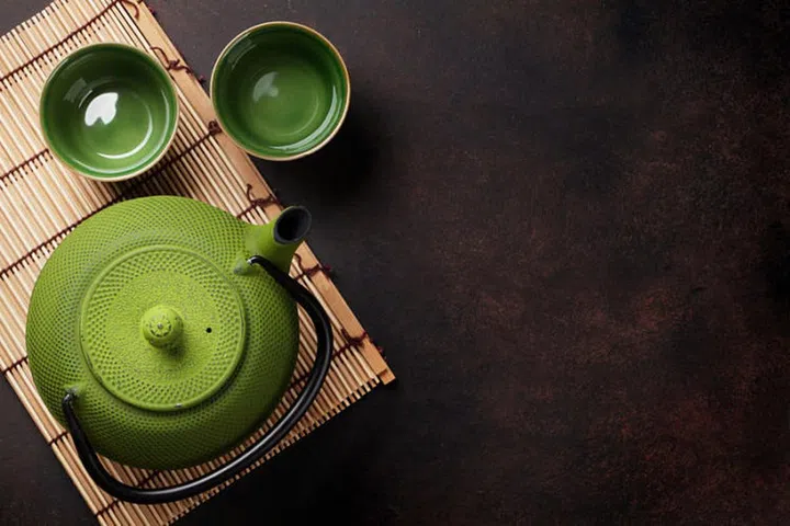 Green teapot and tea cups on stone table. Top view with copy space