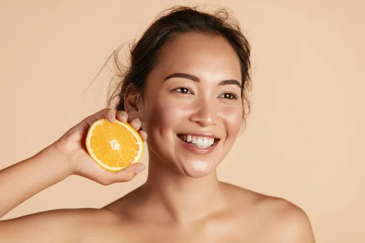 Beauty. Smiling woman with radiant face skin and orange portrait. Beautiful smiling asian girl model with natural makeup, healthy smile and glowing hydrated facial skin. Vitamin C cosmetics concept