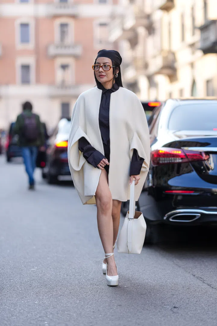 MILAN, ITALY - FEBRUARY 27: A guest wears black head scarf, dark brown sunglasses, silver earrings, black long sleeve shirt, cream wool cape, white leather bag, white platform heels leather shoes, outside Max Mara, during the Milan Fashion week Women's Fall/Winter 2025-2026 on February 27, 2025 in Milan, Italy. (Photo by Edward Berthelot/Getty Images)