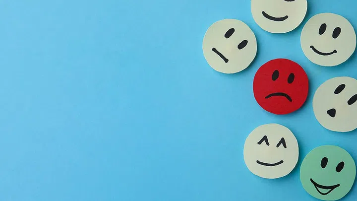 Many faces with different emotions on light blue background, flat lay. Space for text